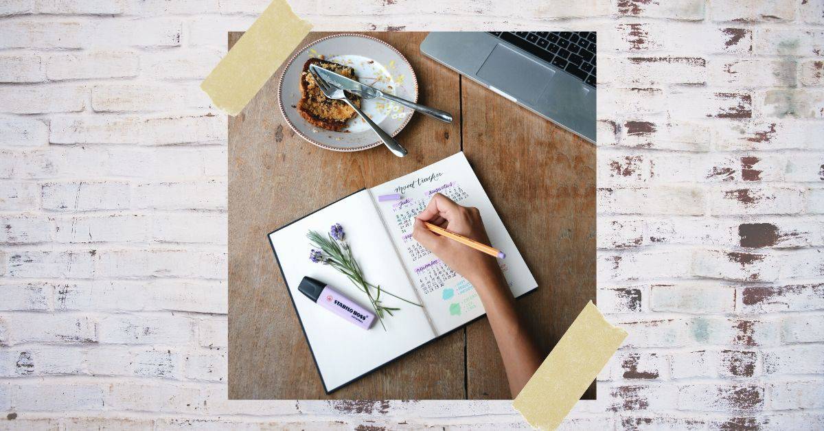 woman writing in journal next to computer